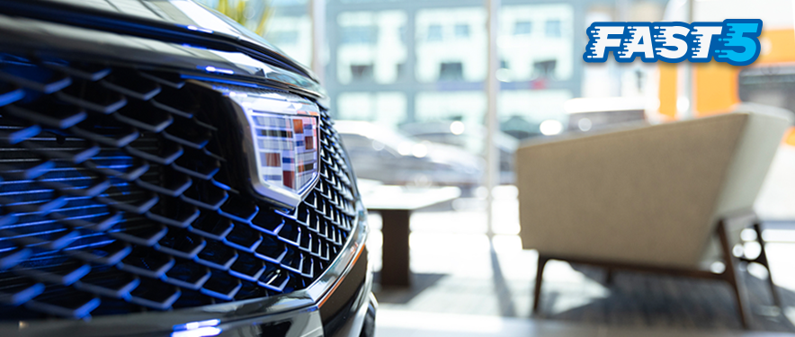 Close-up of a Cadillac grill inside a dealership with FAST 5 in the top-right corner